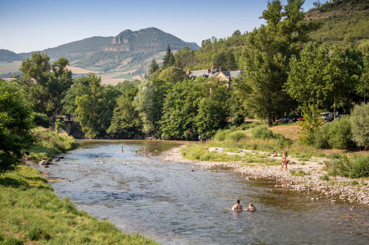 Site de vacances Huttopia Millau en Occitanie, France, avec rivière, baigneurs et collines verdoyantes.