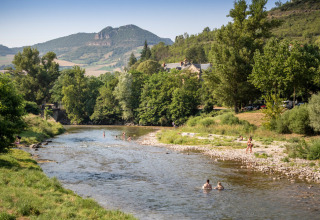 Huttopia Millau vakantiepark in Occitanië, Frankrijk, met rivier, zwemmers en bosrijke heuvels.