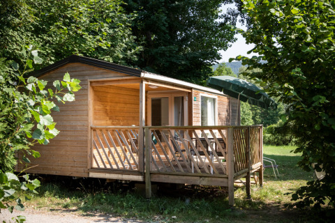 Cabaña de madera con terraza y sombrilla en Huttopia Millau, parque vacacional en Occitania rodeado de naturaleza.