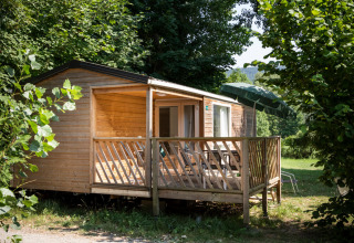 Træhytte med terrasse og parasol ved Huttopia Millau feriepark omgivet af grøn natur i Occitanie, Frankrig.