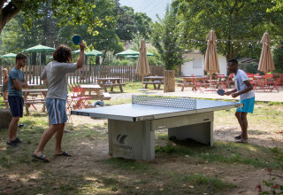 Bezoekers spelen buiten pingpong in vakantiepark Huttopia Millau in Occitanië, Frankrijk, tussen de bomen.