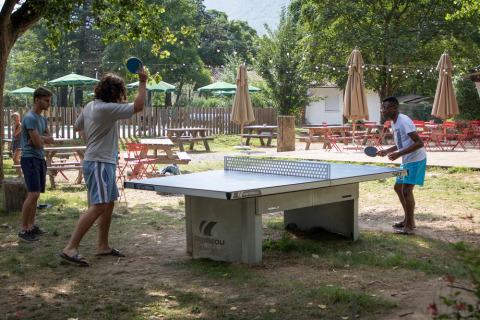 Gäste spielen Tischtennis im Freien im Ferienpark Huttopia Millau in Occitanie, Frankreich bei Bäumen.