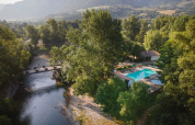 Luftfoto af ferieparken Huttopia Millau i Occitanie, Frankrig, med pool, flod og bjerge i baggrunden.