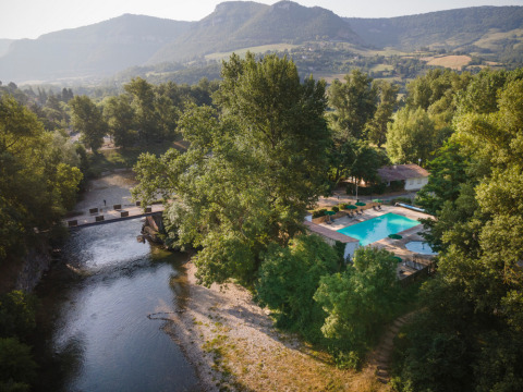 Aerial view of Huttopia Millau holiday park in Occitanie, France, featuring a pool, river, and lush mountains.