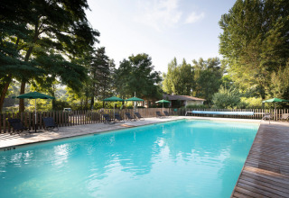 Udendørs swimmingpool med liggestole og grønne parasoller i ferieparken Huttopia Millau, Occitanie, Frankrig.