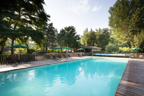 Piscina al aire libre con tumbonas y sombrillas verdes en Huttopia Millau, un parque vacacional en Occitania, Francia.