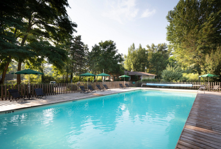 Piscine extérieure avec transats et parasols verts au village vacances Huttopia Millau en Occitanie, France.