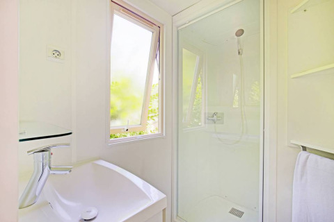 Baño luminoso con cabina de ducha y ventana en una casa móvil en Huttopia Millau, Francia.