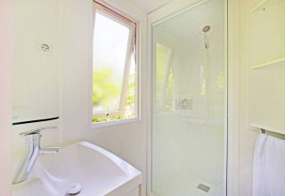 Baño luminoso con cabina de ducha y ventana en una casa móvil en Huttopia Millau, Francia.