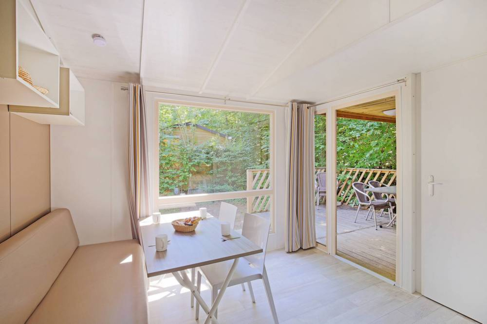 Lichte stacaravan Cottage bij Huttopia Millau, Frankrijk, met eettafel en terras buiten in het groen.