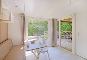 Lys mobilhytte Cottage ved Huttopia Millau i Frankrig med indendørs spisebord og terrasse udenfor.