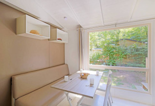 Bright dining area in the Mobile home Cottage at Huttopia Millau, France, overlooking a green garden.
