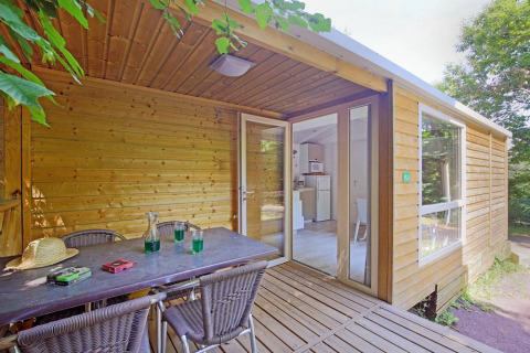 Terraza exterior de una cabaña móvil en Huttopia Millau, Francia, con mesa, sillas y vista al bosque.