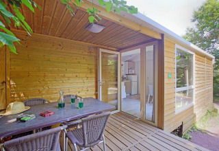 Terraza exterior de una cabaña móvil en Huttopia Millau, Francia, con mesa, sillas y vista al bosque.