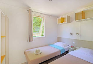 Foto interna di una Mobile home Cottage a Huttopia Millau, Francia, con due letti singoli e finestra luminosa.