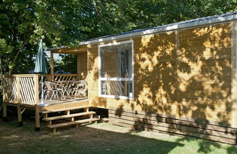 Mobilhjem Cottage ved Huttopia Millau i Frankrig, med terrasse, stole og grøn parasol under træer.