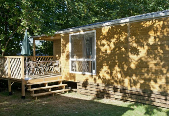 Mobilhjem Cottage ved Huttopia Millau i Frankrig, med terrasse, stole og grøn parasol under træer.