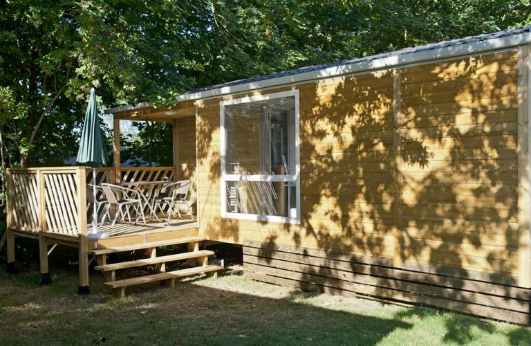 Casa móvil Cottage en Huttopia Millau, Francia, con terraza de madera, sillas y sombrilla verde.