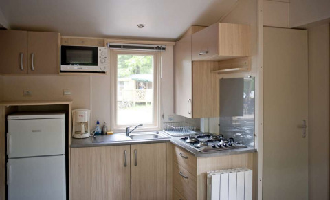 Lyst køkken i Mobile home Cottage på Huttopia Millau i Frankrig, med komfur, vask, køleskab og mikroovn.