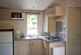 Cocina luminosa en la Mobile home Cottage de Huttopia Millau, Francia, con estufa, fregadero y refrigerador.