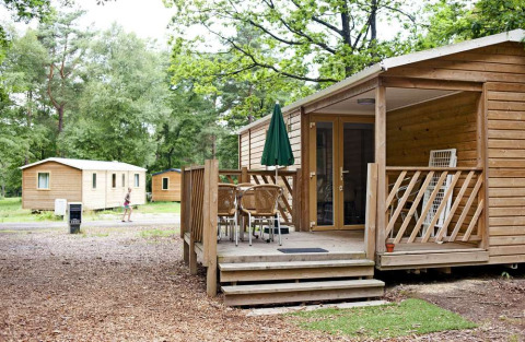 Træhytte med terrasse og havemøbler i skovmiljø ved Mobile Home Cottage på Huttopia Millau, Frankrig.