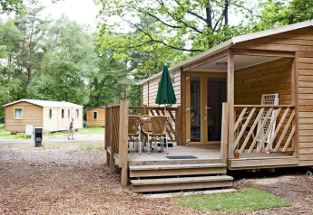 Wooden cabin with covered terrace and outdoor dining set at Mobile Home Cottage, Huttopia Millau, France.