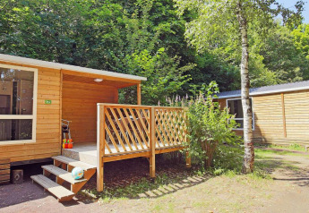 Mobilhjem Cottage på Huttopia Millau i Frankrig, omgivet af frodige grønne træer og naturlig skov.