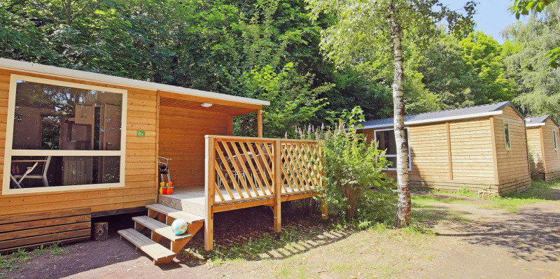 Casa móvil Cottage en Huttopia Millau, Francia, rodeada de árboles verdes y naturaleza tranquila del bosque.