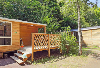Mobile Home Cottage im Huttopia Millau, Frankreich, umgeben von grünen Bäumen und ruhiger Natur.