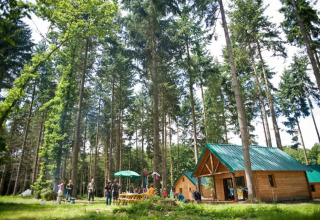 Gezinnen genieten in het bos bij houten hutten met groene daken in Village Huttopia Senonches, Frankrijk.
