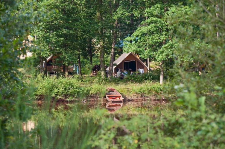 Peaceful campsite at Huttopia Senonches, Centre-Val de Loire, France, with tents by the forest and a canoe by the lake.