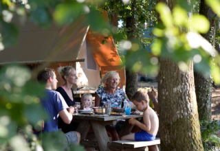 Famiglia si gode un pasto al tavolo da picnic nei boschi di Village Huttopia Senonches, Centre-Val de Loire, Francia.