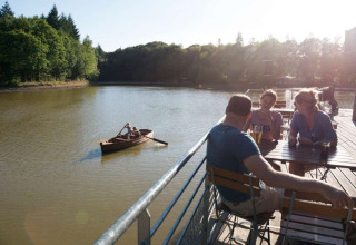 Mensen genieten van drankjes op een terras bij het meer in Village Huttopia Senonches, Centre-Val de Loire, Frankrijk.