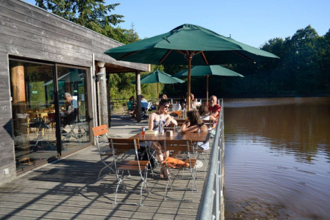 Terraza al aire libre junto al lago en Village Huttopia Senonches, Centre-Val de Loire, Francia, con visitantes.