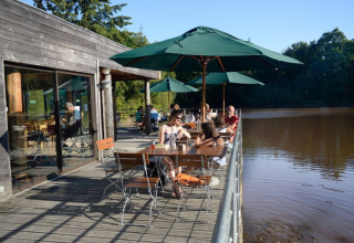 Terraza al aire libre junto al lago en Village Huttopia Senonches, Centre-Val de Loire, Francia, con visitantes.
