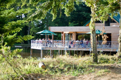 Personas disfrutando en una terraza de madera junto al lago en Village Huttopia Senonches, Centro-Val de Loire.