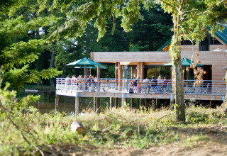 Mensen genieten op een houten terras met uitzicht op het meer bij Village Huttopia Senonches, Frankrijk.