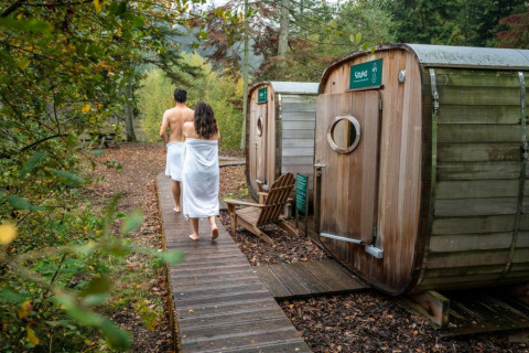 Pareja caminando hacia saunas en Village Huttopia Senonches, un parque de vacaciones en Centre-Val de Loire, Francia.