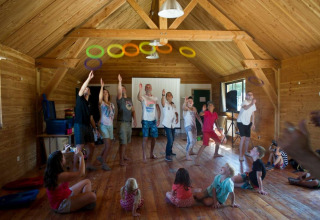 Kinder und Erwachsene spielen mit bunten Ringen in einer Holzhütte im Village Huttopia Senonches, Frankreich.