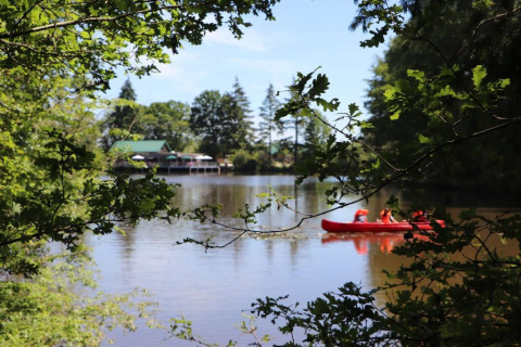 Vista al lago en Village Huttopia Senonches, Francia, con una canoa roja y árboles verdes alrededor.