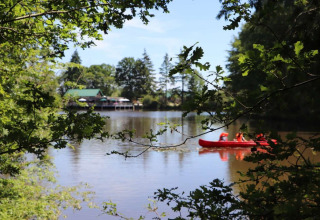 Vista sul lago al Village Huttopia Senonches, Francia, con una canoa rossa e alberi verdi intorno.