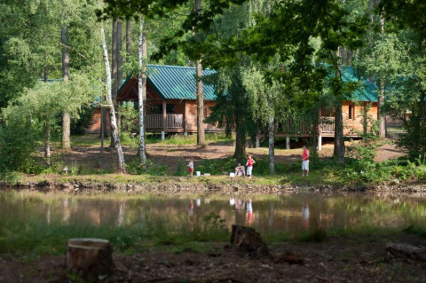 Familie beim Angeln am Teich vor Holzhütten im Village Huttopia Senonches, einem Ferienpark in Frankreich.