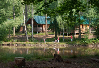 Family by the pond in front of wooden cabins at Village Huttopia Senonches holiday park, Centre-Val de Loire, France.