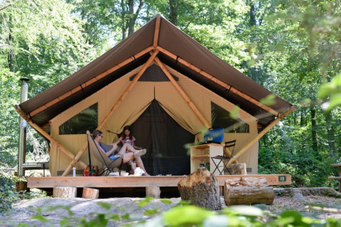 Due persone si rilassano davanti a una tenda glamping a Village Huttopia Senonches, Centre-Val de Loire.