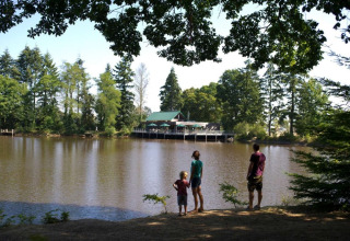 Familie nyder udsigt til sø og træer ved Village Huttopia Senonches feriepark i Centre-Val de Loire, Frankrig.