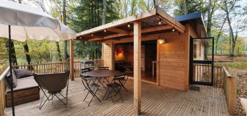 Terraza de madera con mesa, sillas y sombrilla al aire libre en Village Huttopia Senonches, Centre-Val de Loire, Francia.