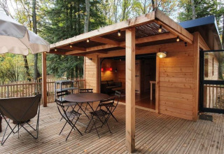 Houten terras met zitplaatsen, tafel en parasol bij Village Huttopia Senonches, Centre-Val de Loire, Frankrijk.