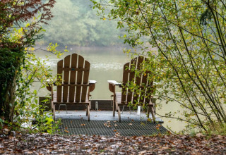 Due sedie di legno su un molo al lago, circondate dal verde a Village Huttopia Senonches, Francia.