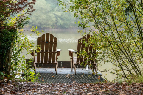 Dos sillas de madera en un muelle junto al lago, rodeadas de vegetación en Village Huttopia Senonches, Francia.