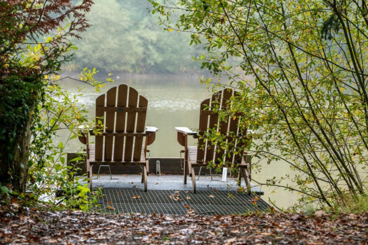 Two wooden chairs on a dock by the lake, surrounded by greenery at Village Huttopia Senonches, France.